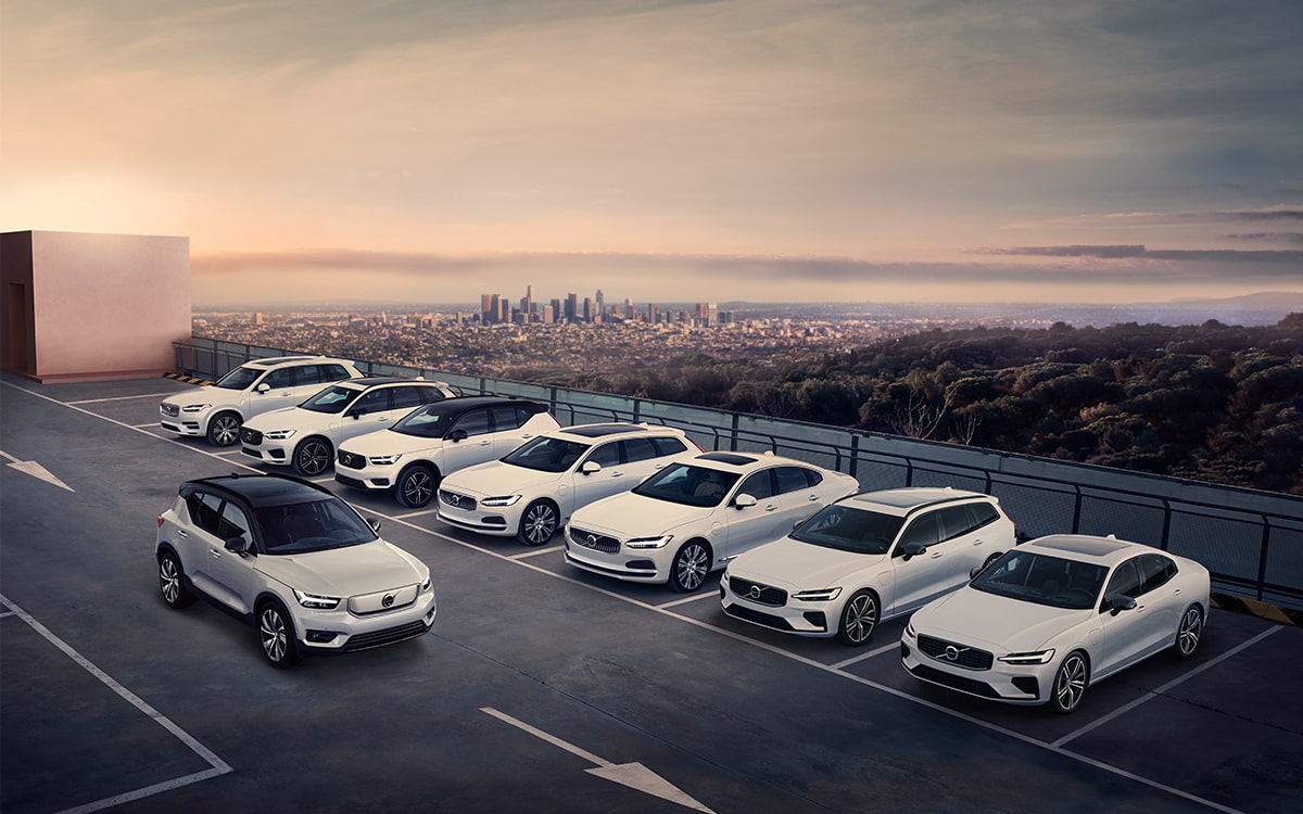 A row of modern, white Volvo company cars parked on a rooftop car park overlooking a city